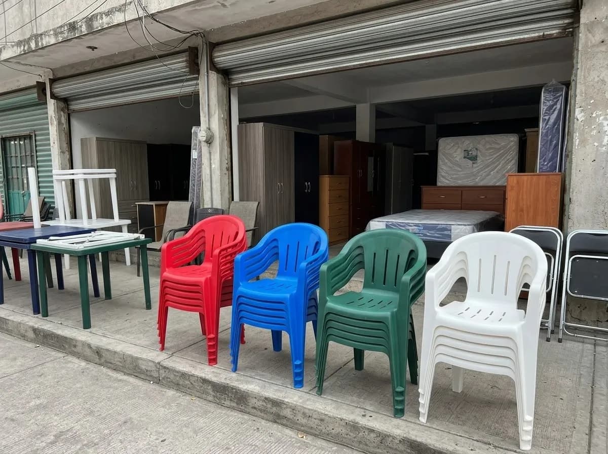 Pilas de sillas roja, azul, verde y blanca en la banqueta frente a una mueblería